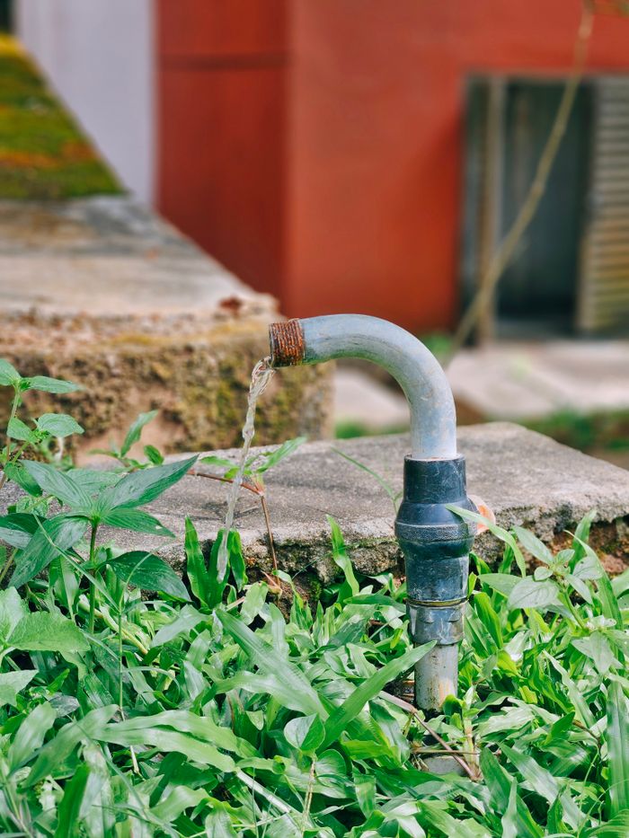 A flowing water pipe surrounded by lush green grass and a concrete platform in an outdoor setting.